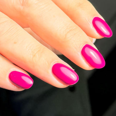 Close-up of a hand with bright pink nail polish on a blurred background